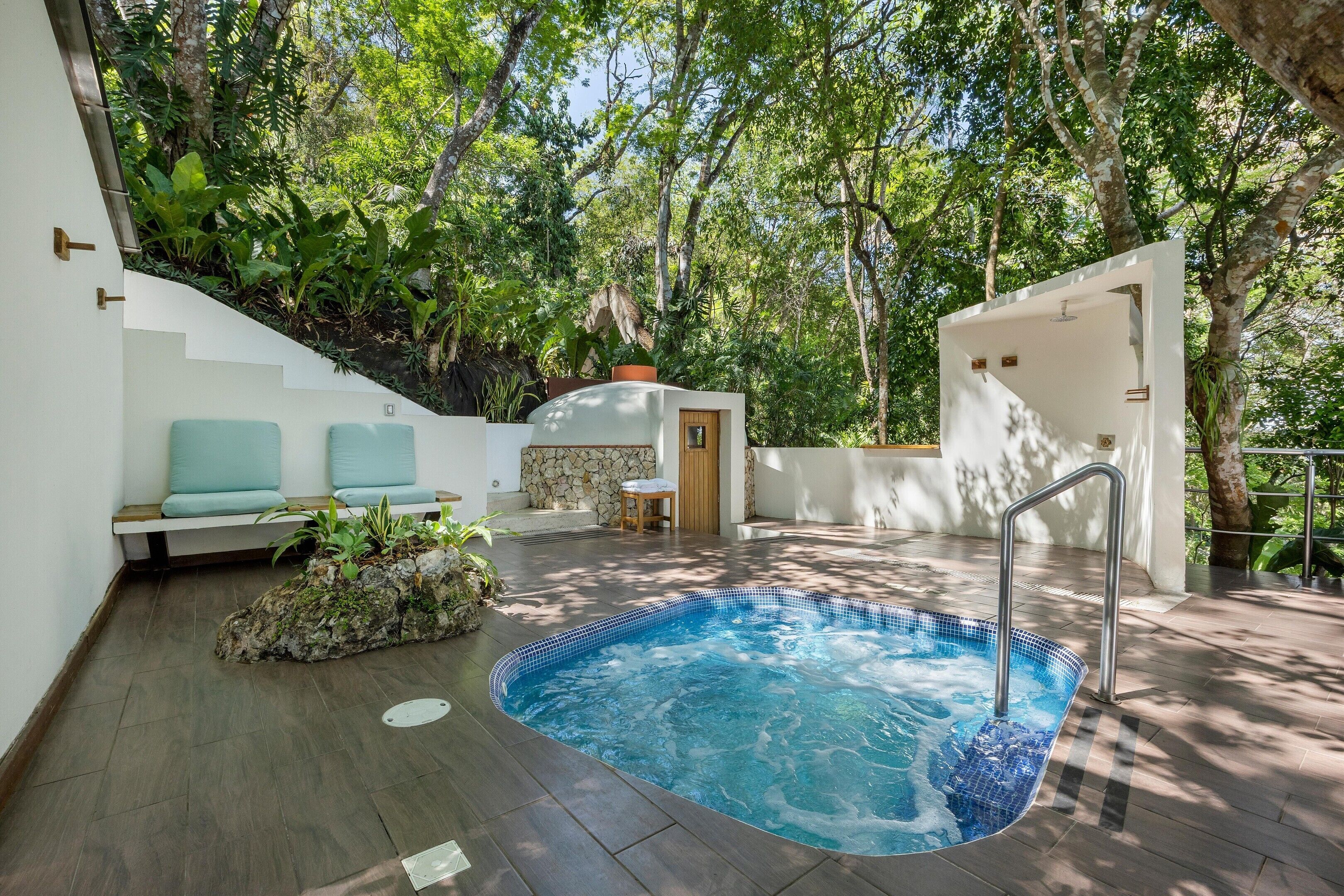 Un área de piscina con un jacuzzi, asientos y una escalera que lleva a un muro de piedra.