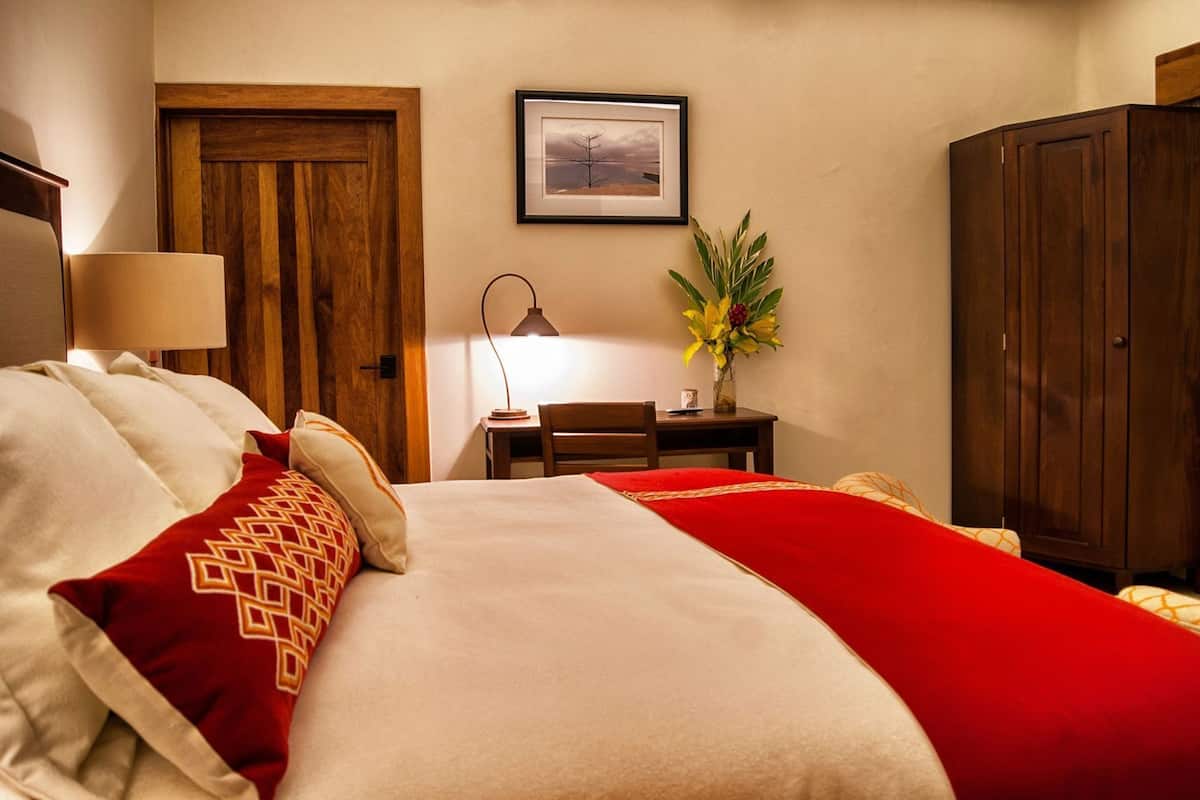 Quarto de hotel com cama, escrivaninha, cadeira, abajur, guarda-roupa e um quadro na parede.