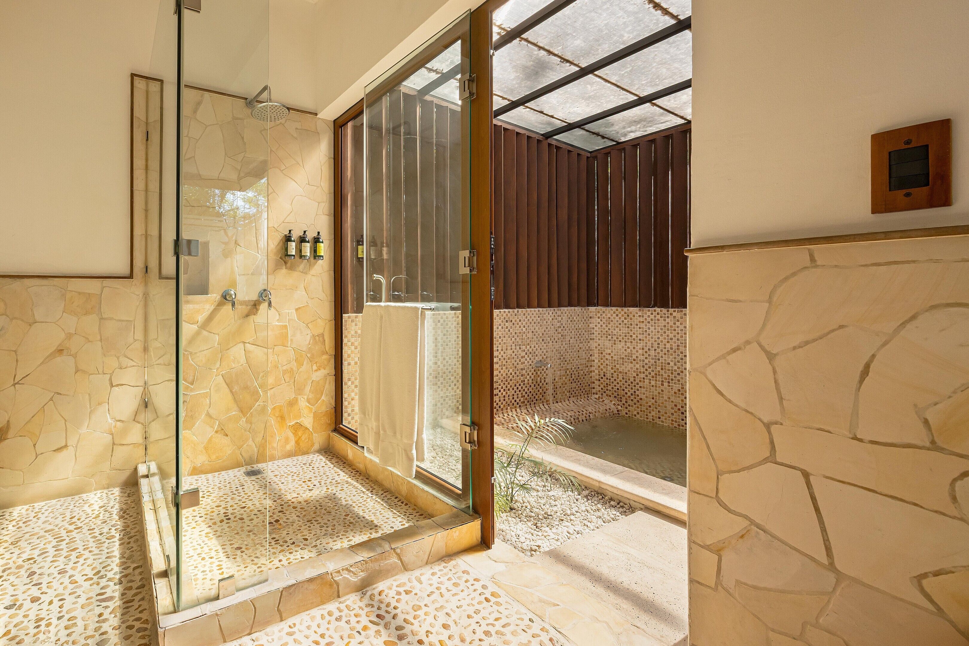 A modern bathroom with a glass-enclosed shower, stone walls, and a wooden panel wall.