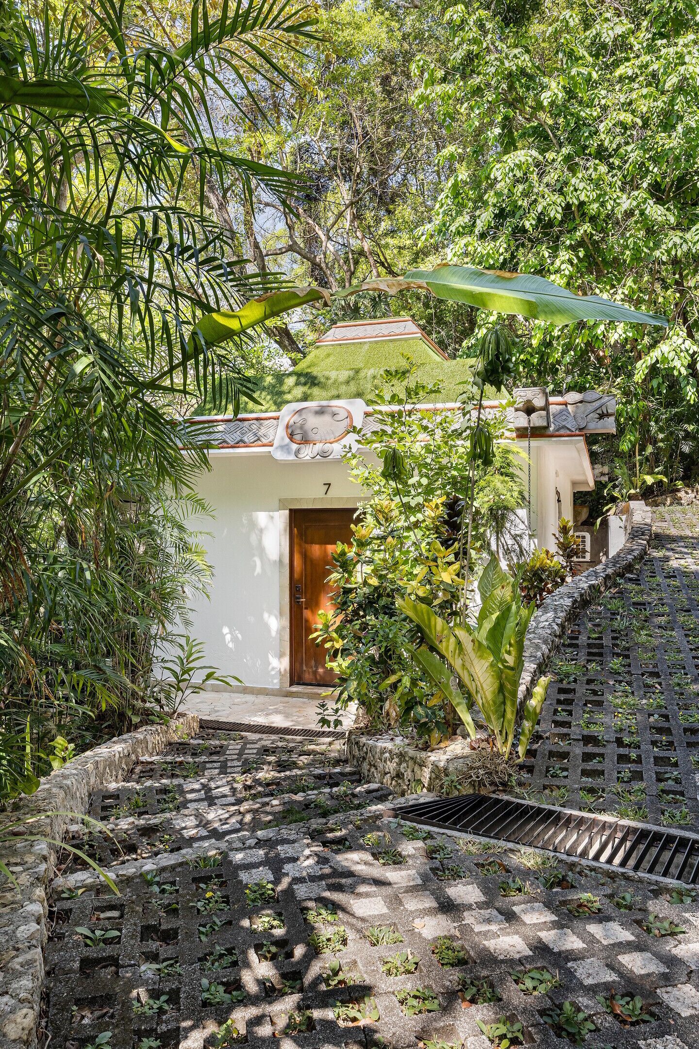 A pathway leading to a building with a number 7 sign, surrounded by lush greenery.