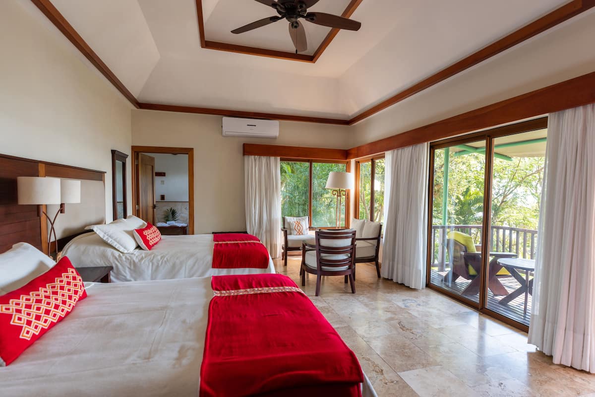 Quarto de hotel com duas camas, varanda e área de estar com mesa e cadeiras.