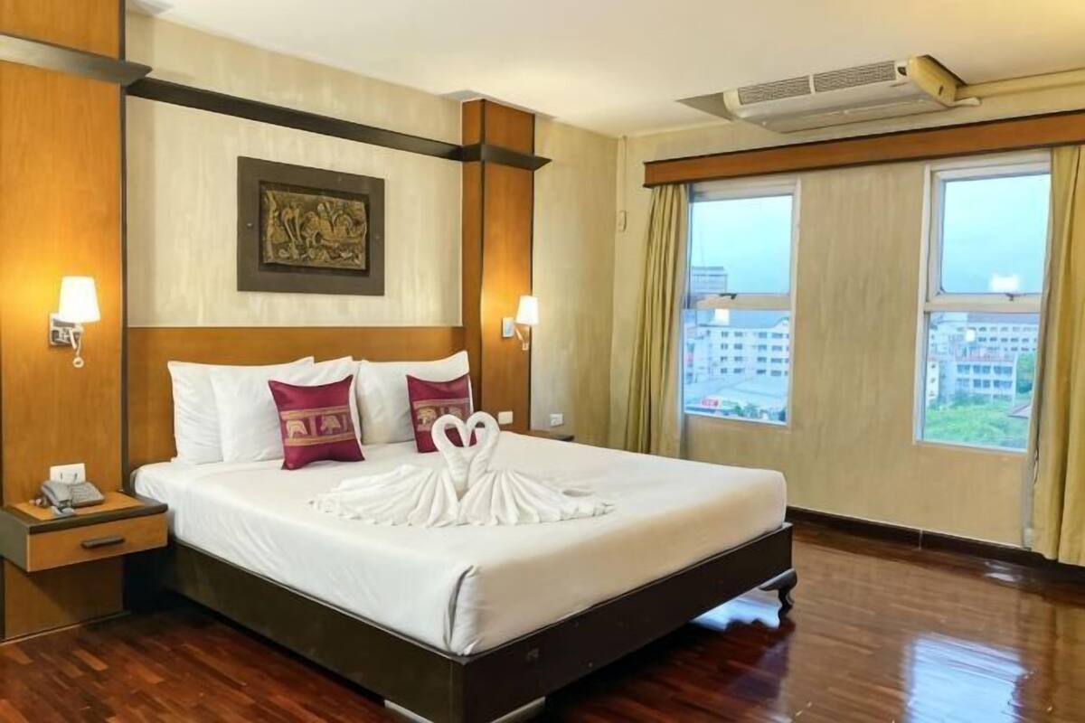 Une chambre d’hôtel avec un grand lit, deux tables de chevet, une œuvre d’art accrochée au mur et une fenêtre donnant sur un paysage.