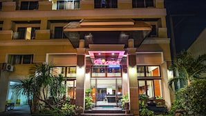 A hotel entrance with a neon sign, a covered entrance area, and surrounding greenery. - Piyada Residence by Nexottel (Pattaya)