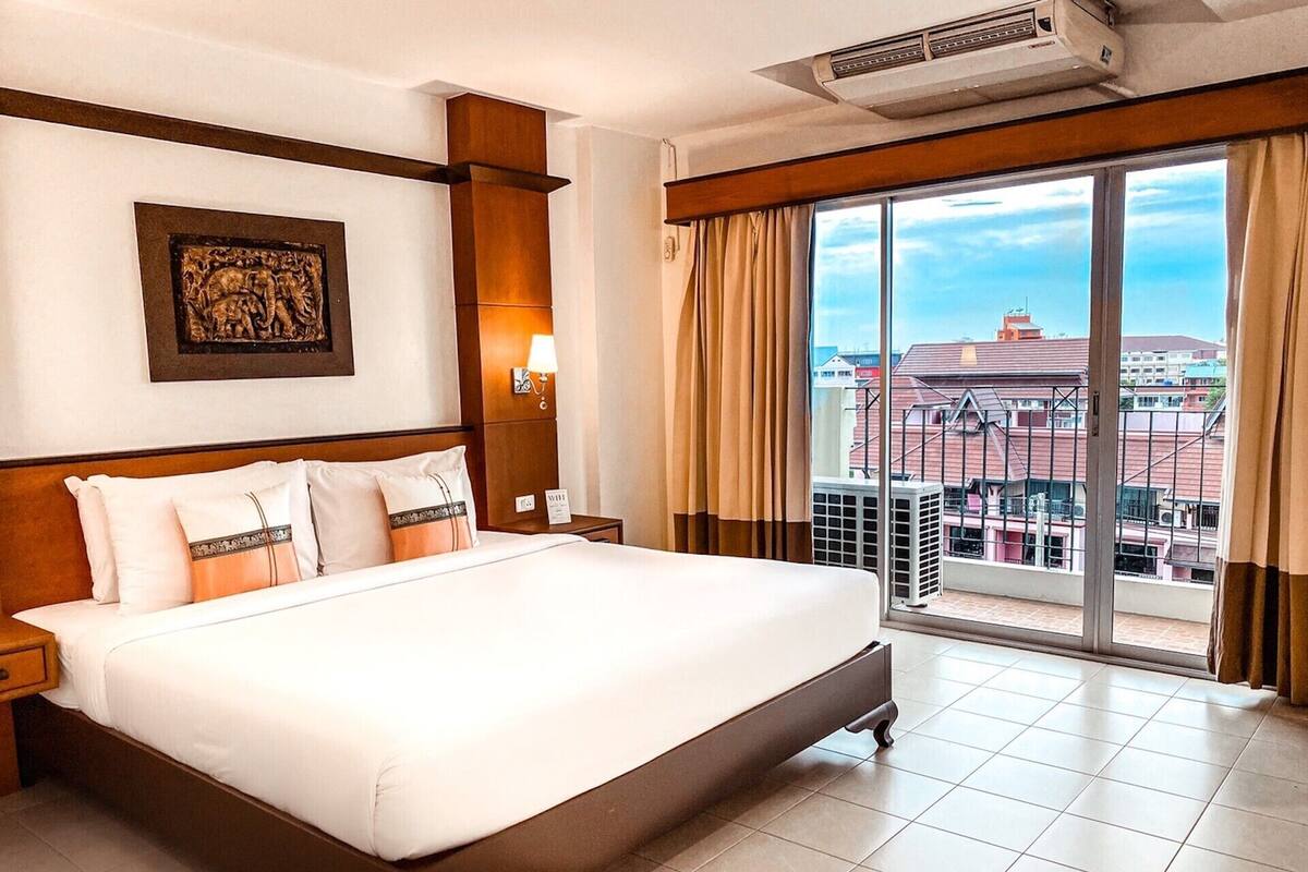 Une chambre d’hôtel avec un grand lit, une table de chevet, une lampe fixée au mur et une grande fenêtre avec des rideaux.