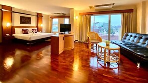 A hotel room with a bed, a sofa, a television, a desk, and a view of the city. - Piyada Residence by Nexottel (Pattaya)