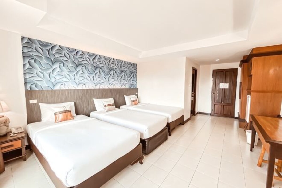 A hotel room with three beds, a wooden headboard, a large wall mural, a wooden desk, and a nightstand.