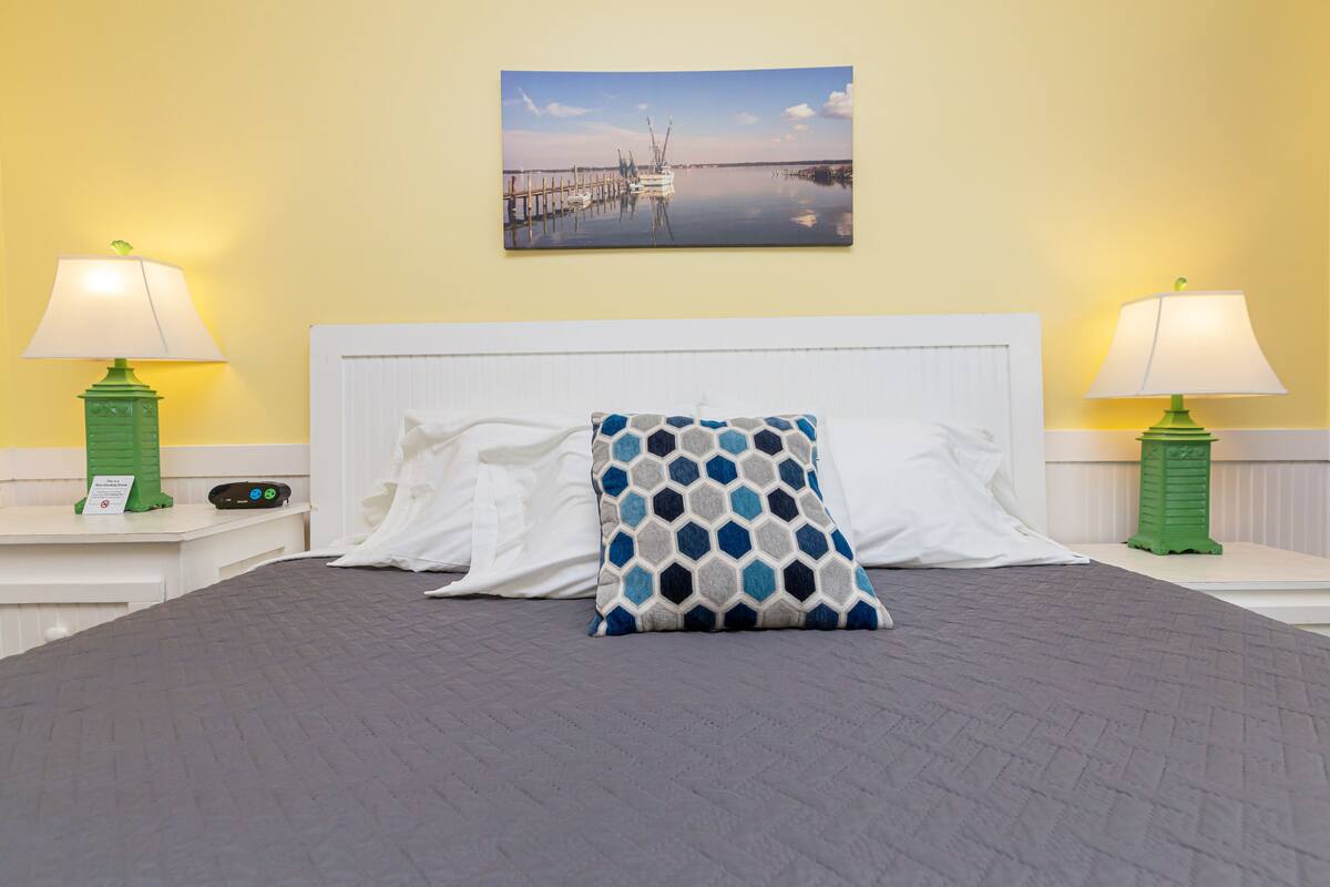 A hotel room with a bed, two nightstands, two lamps, a painting, and a patterned pillow.