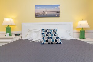 A hotel room with a bed, two nightstands, two lamps, a painting, and a patterned pillow.