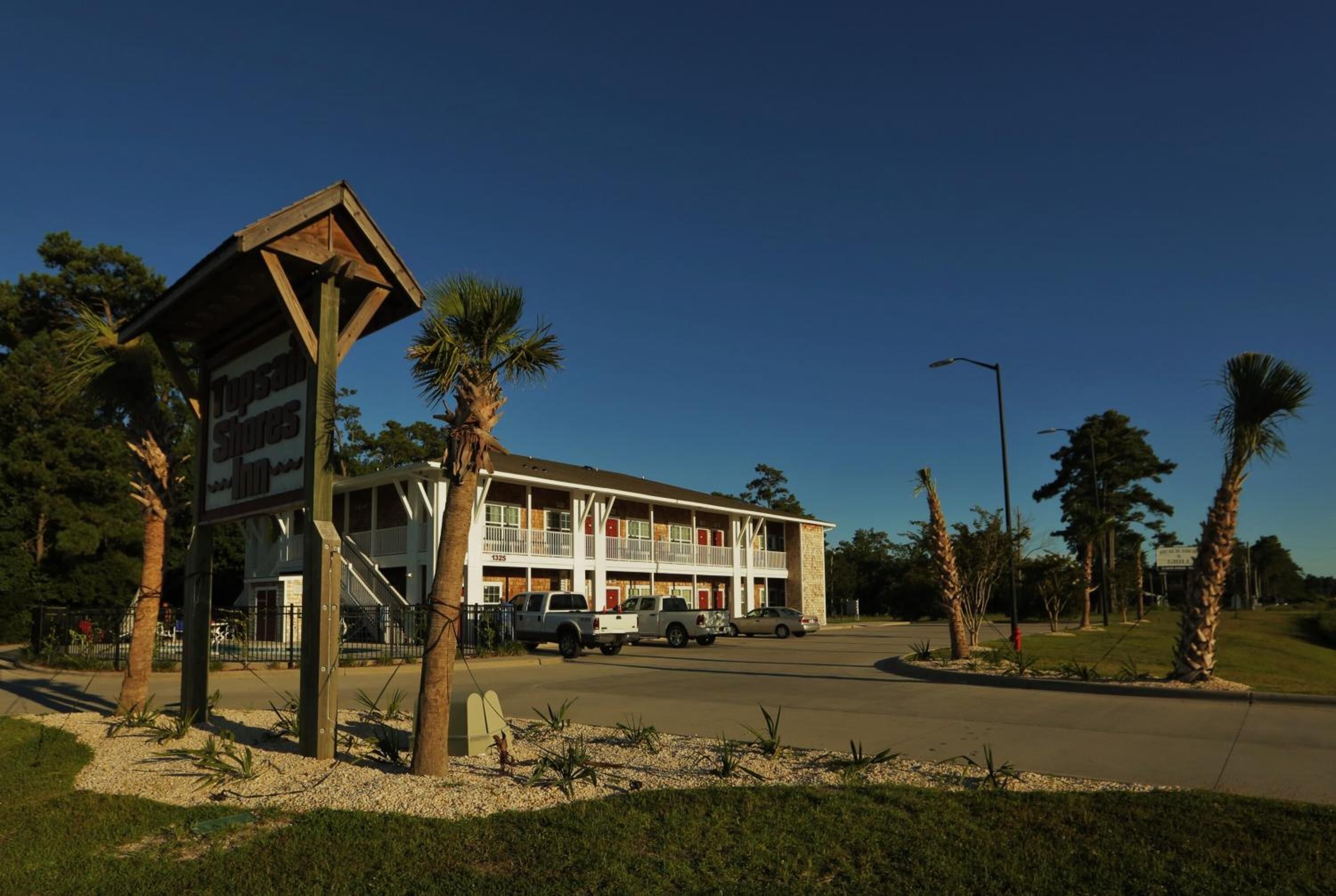 A motel with a two-story structure, a covered parking area, and palm trees in the vicinity.
