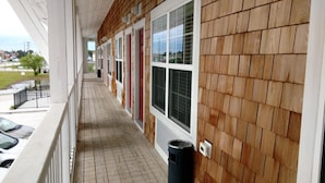 Een overdekt buitengebied met houten bekleding en grote ramen, dat uitkomt op een gebouw met meerdere deuren.