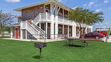 A two-story building with a covered porch, a staircase, and a picnic table in the front yard.