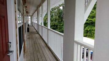 A covered wooden deck with white railings, leading to a door.