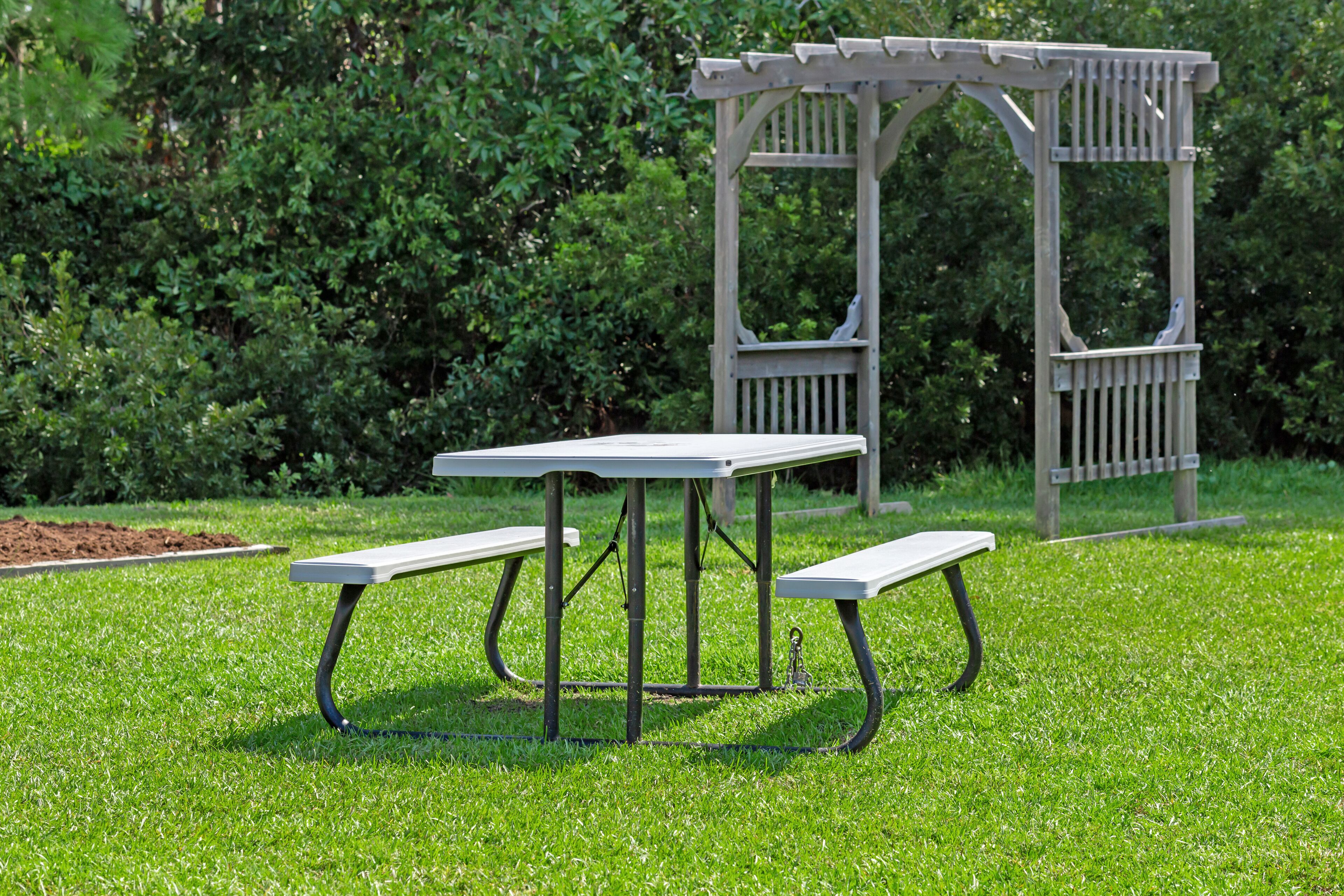 Een picknicktafel met bankjes in een gazon, omgeven door weelderige begroeiing.