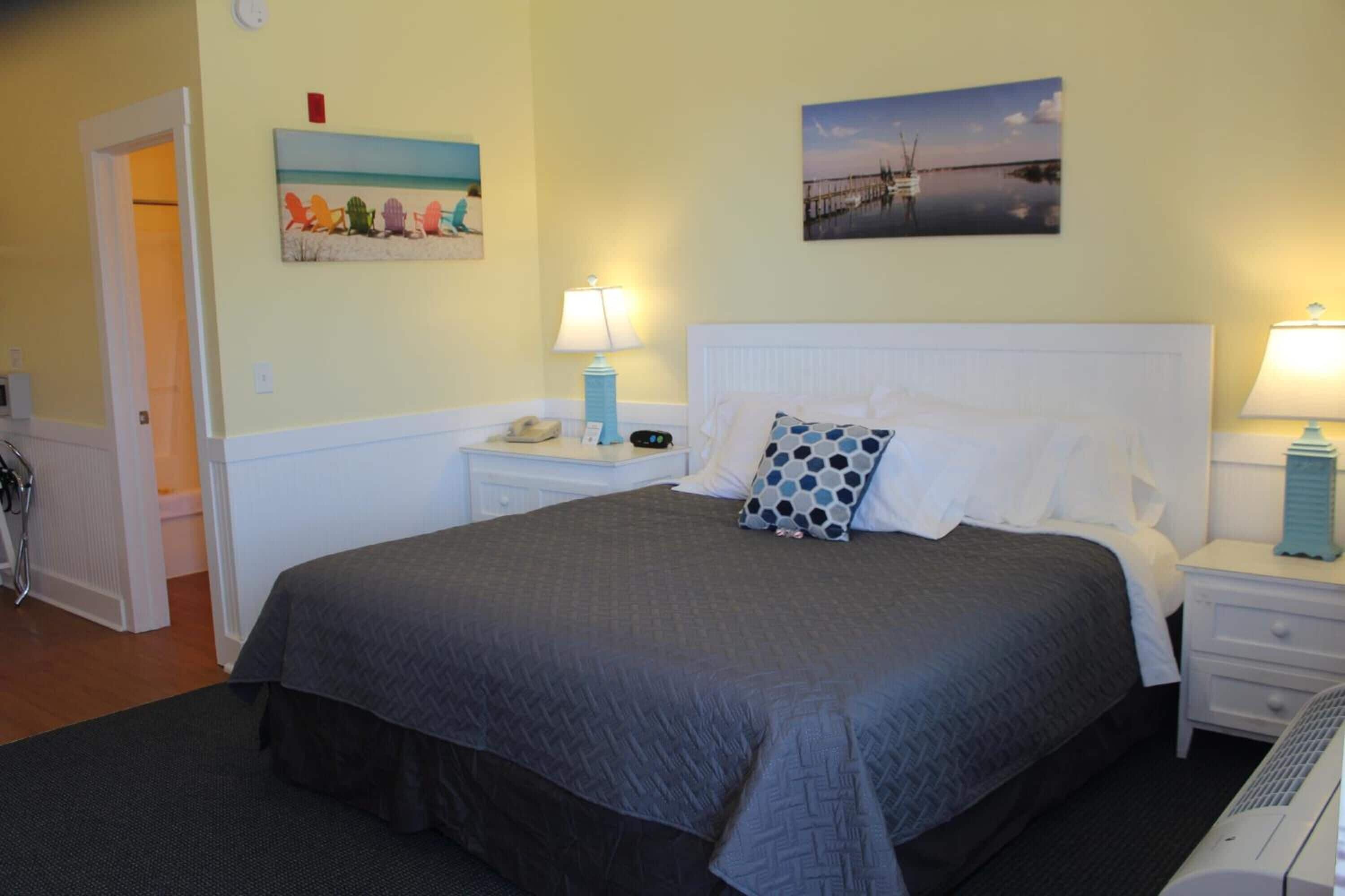 A neatly arranged bedroom with a large bed, two bedside tables, and a nightstand. There are two wall-mounted lamps on each side of the bed. The room has a door leading to another area and a small window.