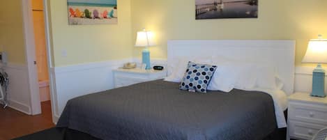 A neatly arranged bedroom with a large bed, two bedside tables, and a nightstand. There are two wall-mounted lamps on each side of the bed. The room has a door leading to another area and a small window.