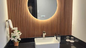 Une salle de bain moderne avec un mur recouvert de panneaux en bois, un miroir rond, un lavabo blanc et une petite plante en pot.