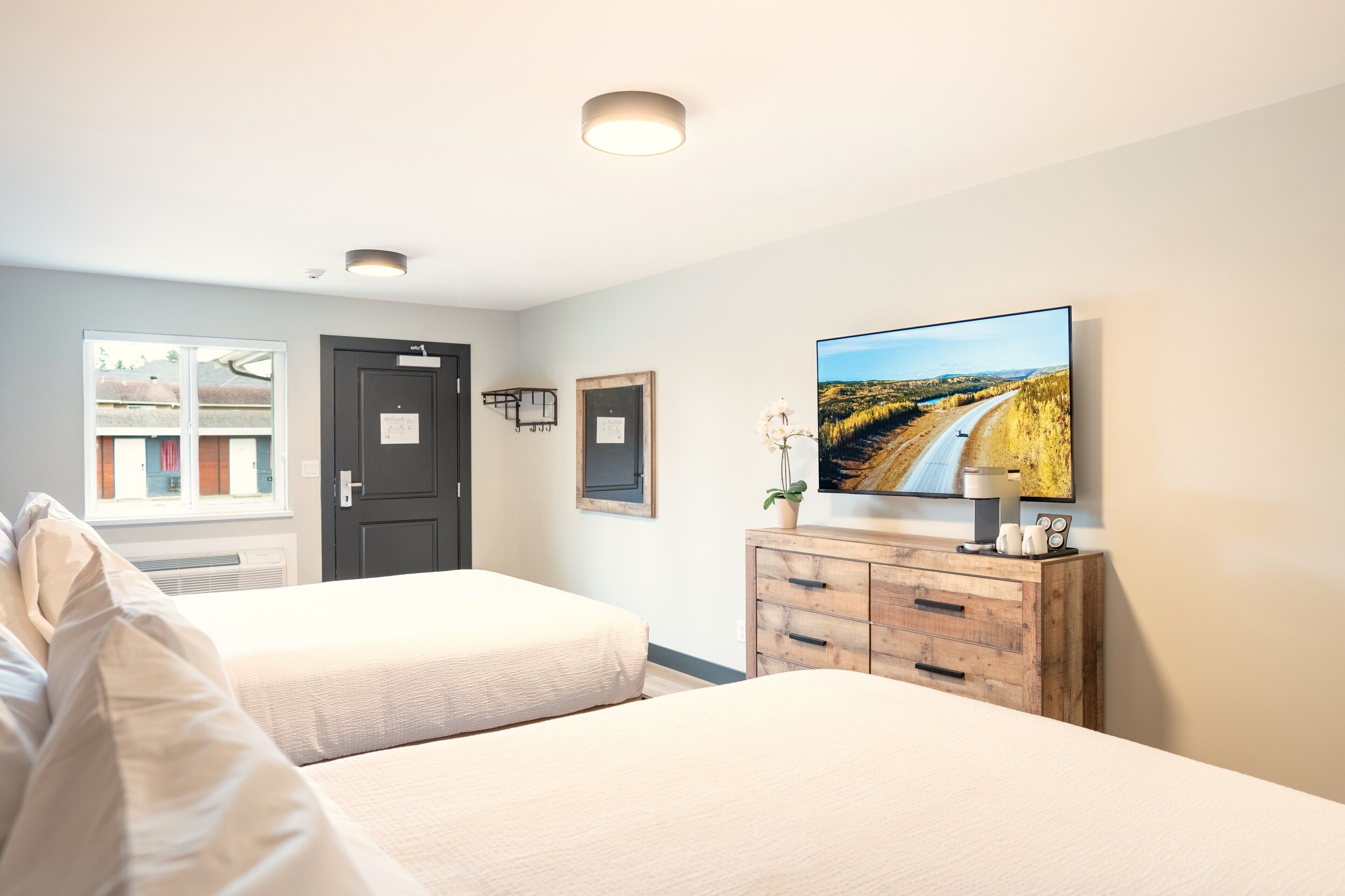 Habitación de hotel con dos camas, un aparador de madera, un televisor de pantalla plana y una ventana con vista a edificios.