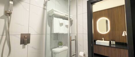 Un baño moderno con ducha de vidrio, inodoro y tocador con espejo.