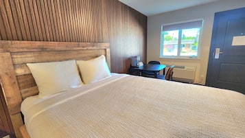 Habitación de hotel con una cama grande, un cabecero de madera, una mesita con una silla y una ventana con vistas al exterior.