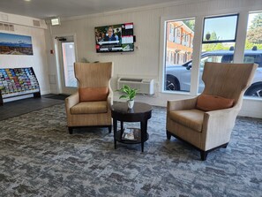 A lobby with two armchairs, a small table with a plant, a TV displaying a news channel, a map display, and a view of the street outside. - Alpine Inn (Abbotsford)