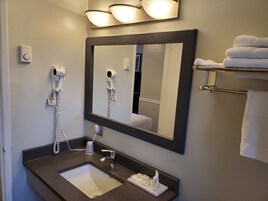 Un baño con lavamanos, espejo, secador de pelo y toallero.