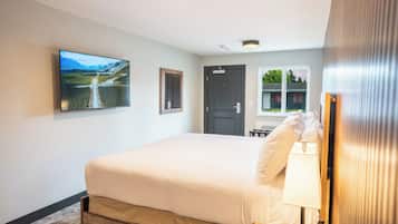 Un dormitorio con cama, televisor montado en la pared, una puerta y una ventana.