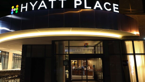 The exterior of a Hyatt Place hotel with a modern design, featuring a prominent illuminated sign and a well-lit entrance.