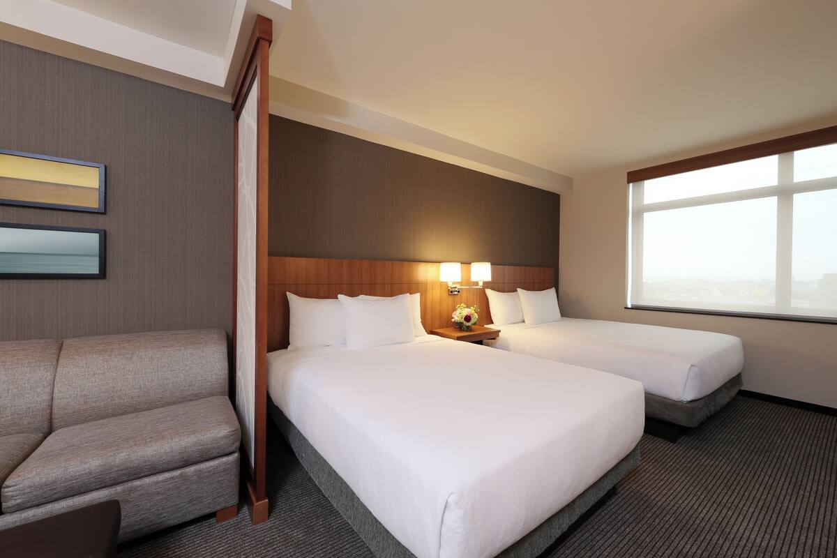 Ein Hotelzimmer mit zwei Betten, einem Schlafsofa und einem großen Fenster.