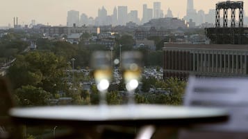 Une vue sur une ville, avec un gratte-ciel imposant visible au loin, prise à travers une fenêtre, avec une table et des chaises au premier plan.