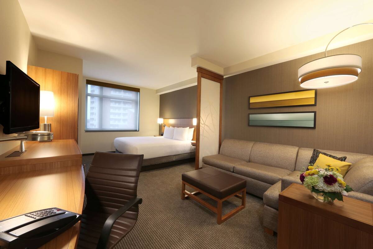 Ein Hotelzimmer mit einem Bett, einem Schreibtisch mit Computer, einer Couch, einem Couchtisch und einem Fernseher.
