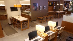 A hotel lobby with multiple seating areas, including a reception desk, several tables and chairs, and a computer station area.