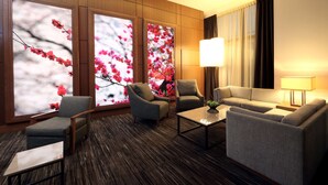 A modern hotel room with a sofa, two armchairs, a coffee table, and large windows with floral views.