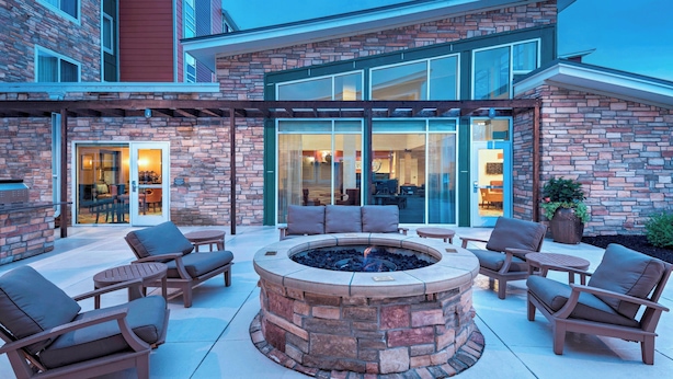 An outdoor patio with a stone fire pit, seating, and a glass door leading to an interior space.