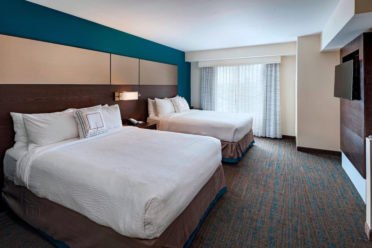 A hotel room with two beds, a TV, and a window with curtains.