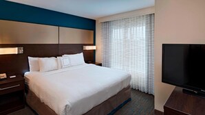A hotel room with a large bed, a TV, a nightstand, and a window with curtains.