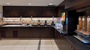 A modern kitchen with dark wood cabinets, a tiled backsplash, and a self-serve breakfast station with various food options.