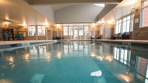 An indoor swimming pool with clear water, surrounded by lounge chairs and a staircase leading to an upper level.