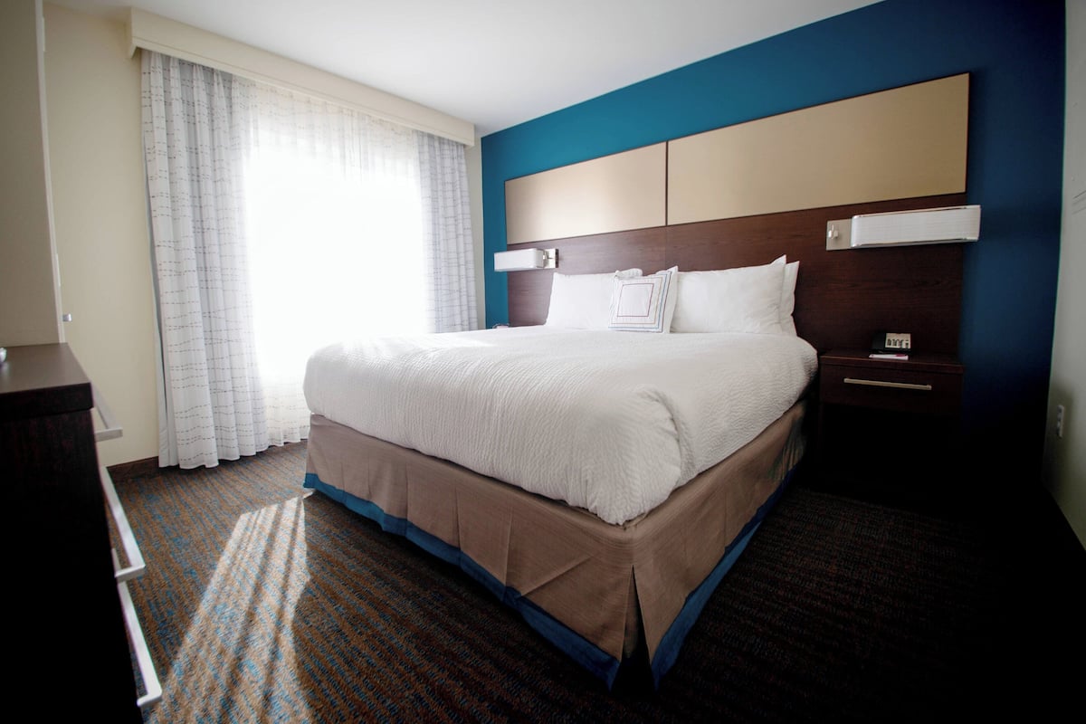 A hotel room with a large bed, a nightstand, a dresser, and a window with curtains.