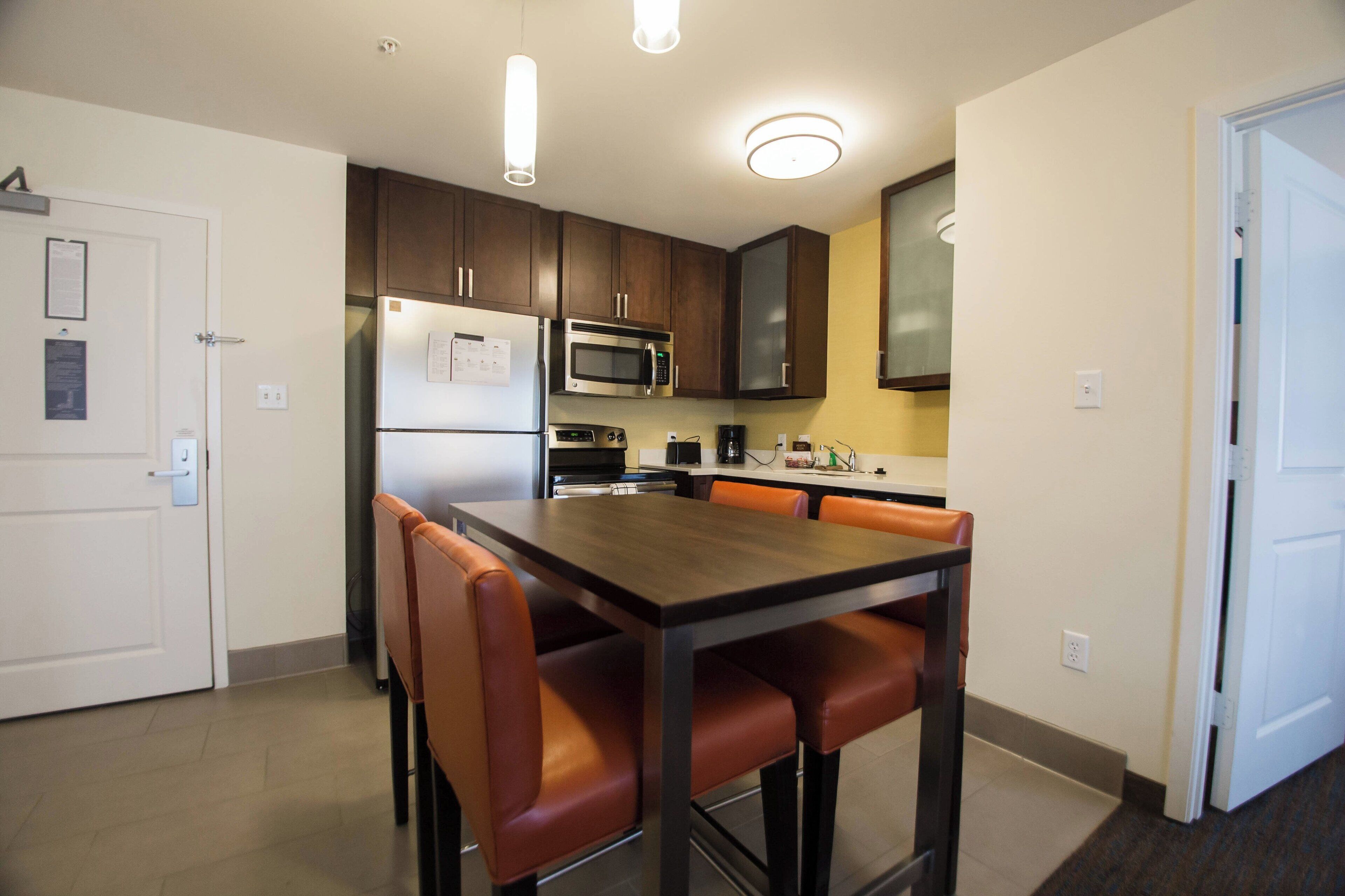 Una cocina moderna con armarios de madera oscura, un refrigerador de acero inoxidable, un microondas y una mesa de comedor con cuatro sillas.