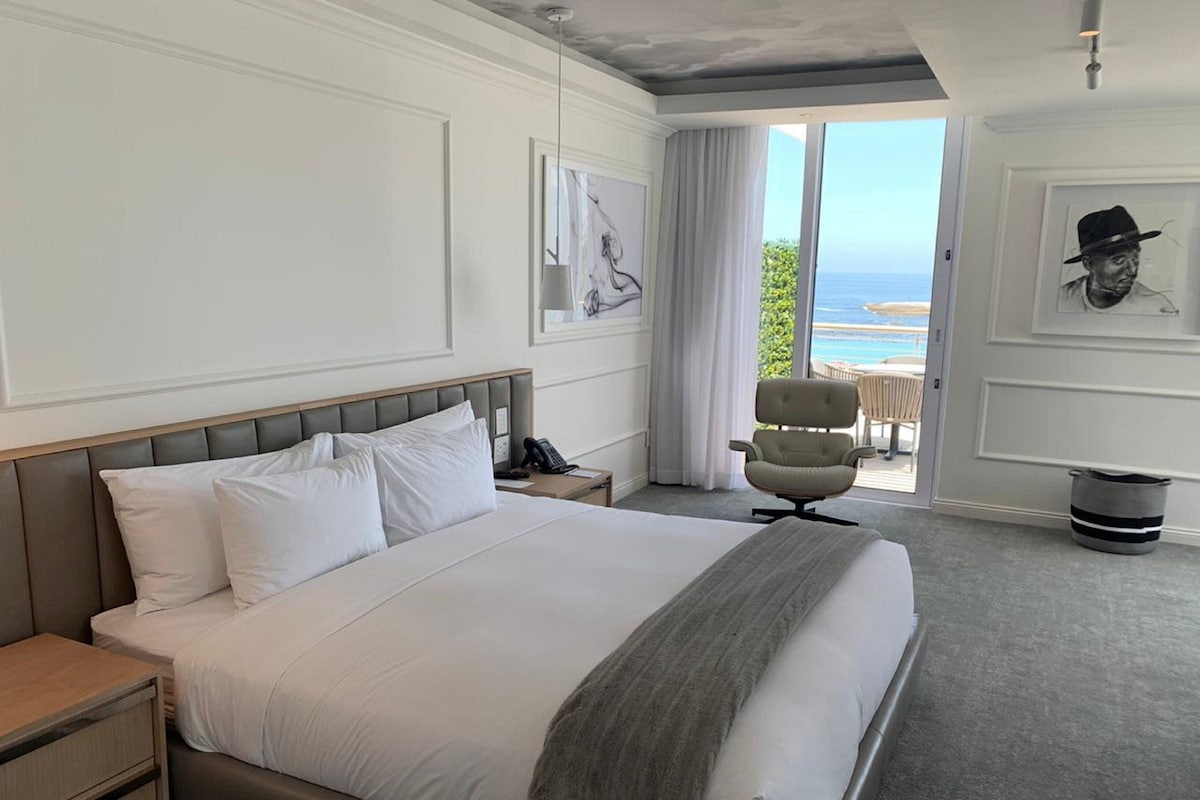 Une chambre d’hôtel avec un grand lit, une table de chevet, une chaise et une vue sur l’océan.