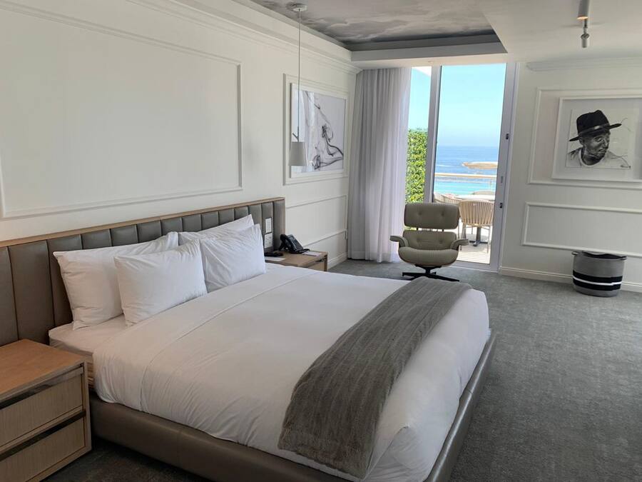 Habitación de hotel con una cama grande, una mesita de noche, una silla y vista al océano.