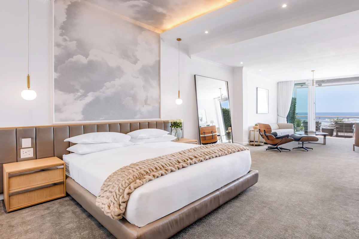 Une chambre d’hôtel moderne dotée d’un grand lit, d’une table de chevet, d’un coin salon avec vue et d’un grand miroir.