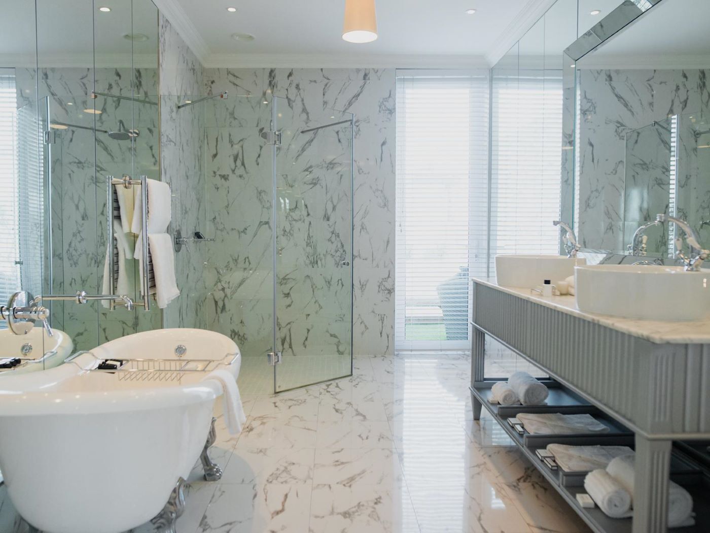 Une salle de bain moderne avec une baignoire sur pieds, un meuble-lavabo doté d'un grand miroir et des murs à motifs de marbre.