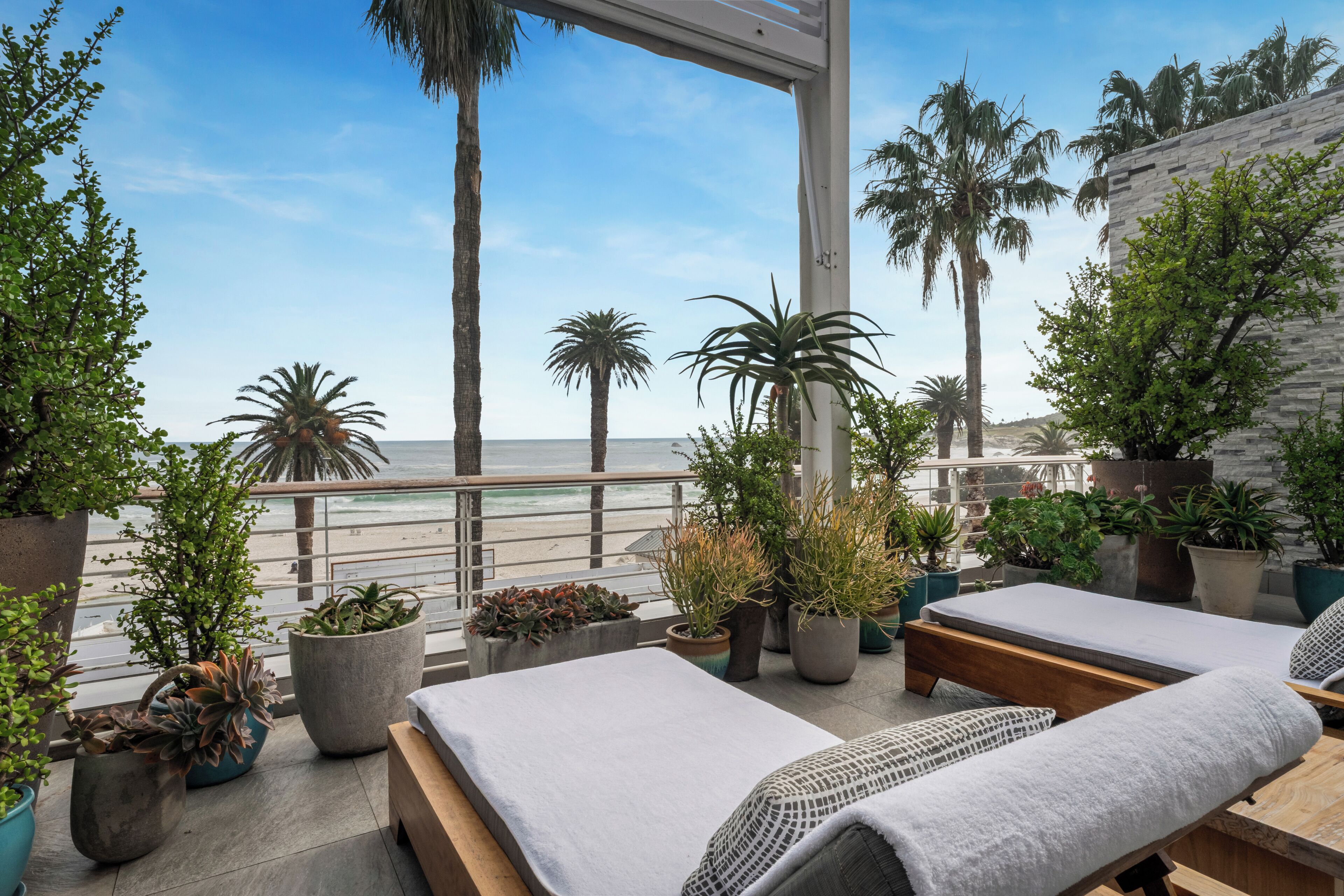 A balcony with a view of the beach, potted plants, and a seating area with a view.
