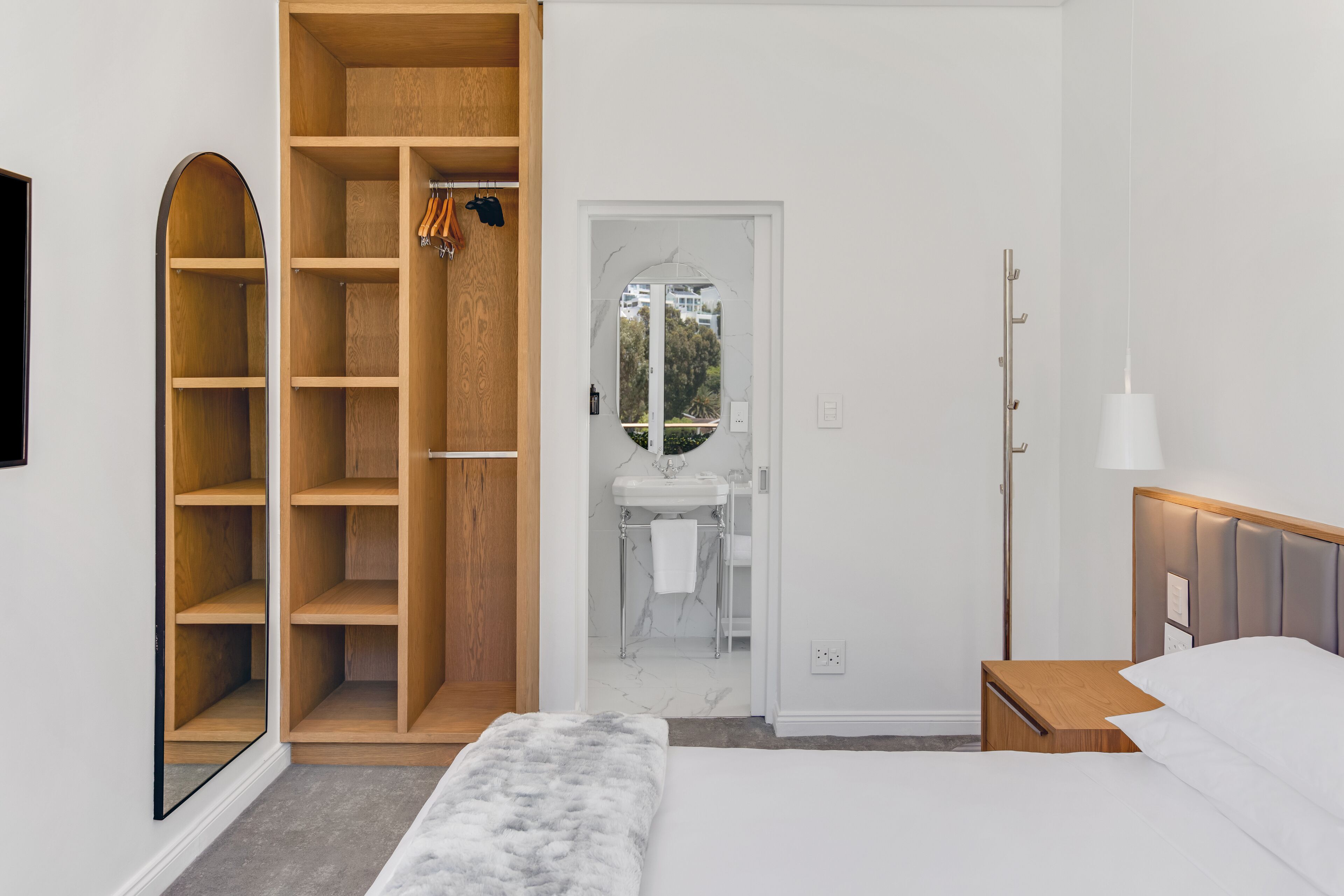 A bedroom with a bed, a wooden wardrobe, a bathroom with a sink, and a mirror.