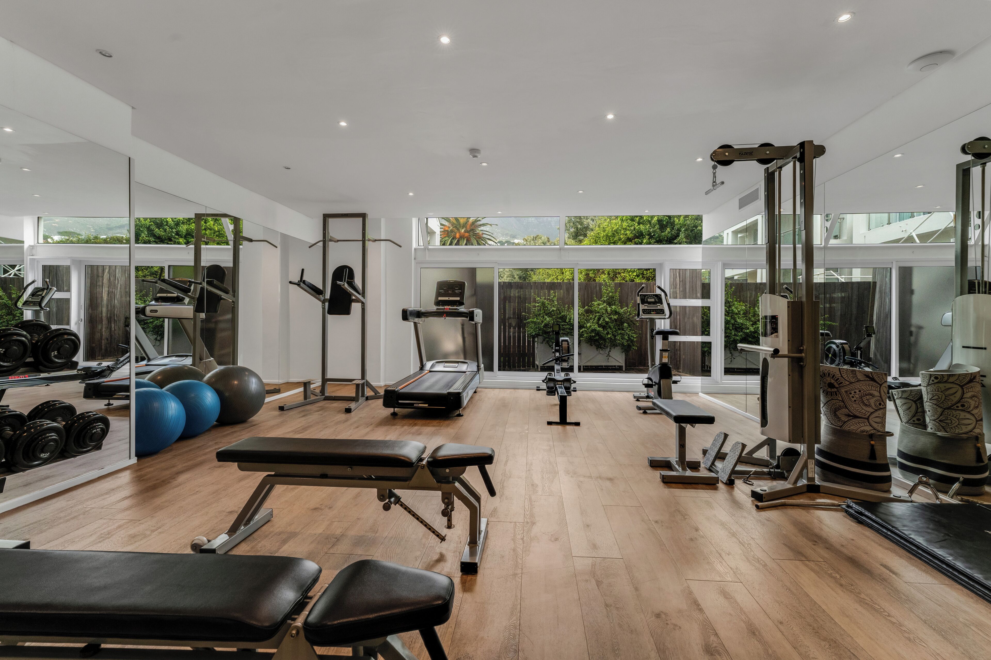 Un gimnasio moderno con diverso equipamiento de ejercicio, amplias ventanas y suelo de madera.