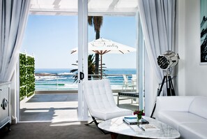 A modern room with a white sofa, a white armchair, a marble coffee table, and a view of the ocean. - The Marly Boutique Hotel & Spa (Cape Town)