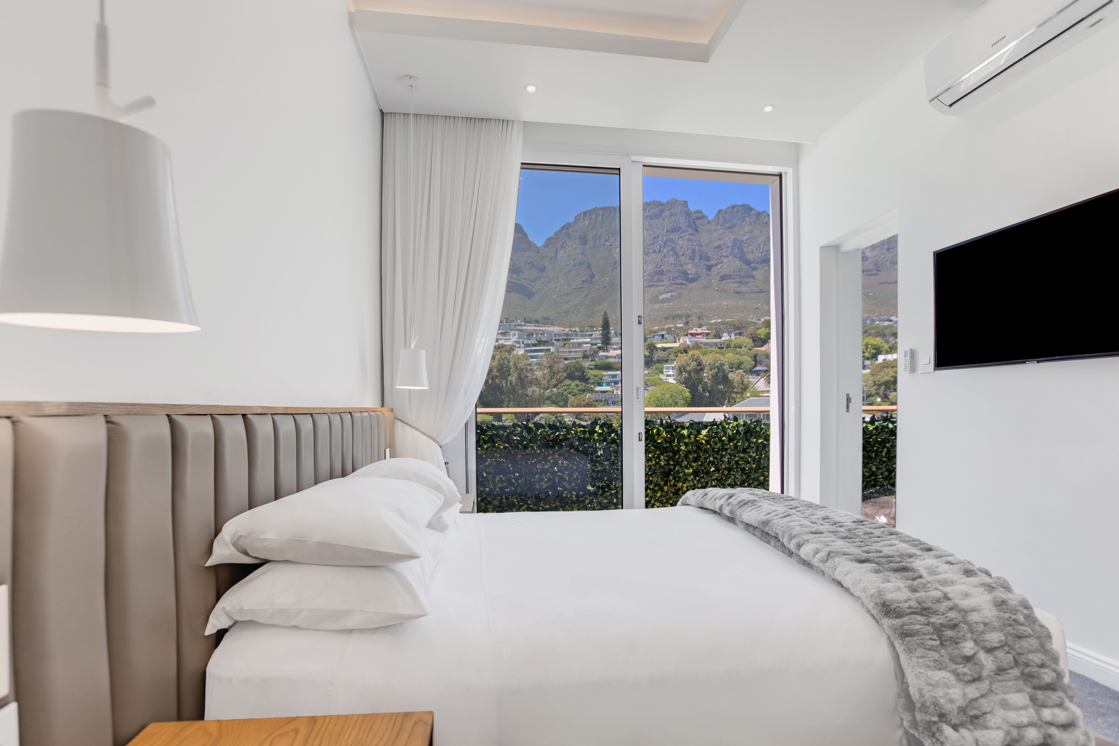 A modern bedroom with a large bed, a flat-screen TV, and a view of mountains.