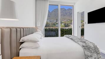 A modern bedroom with a large bed, a flat-screen TV, and a view of mountains.