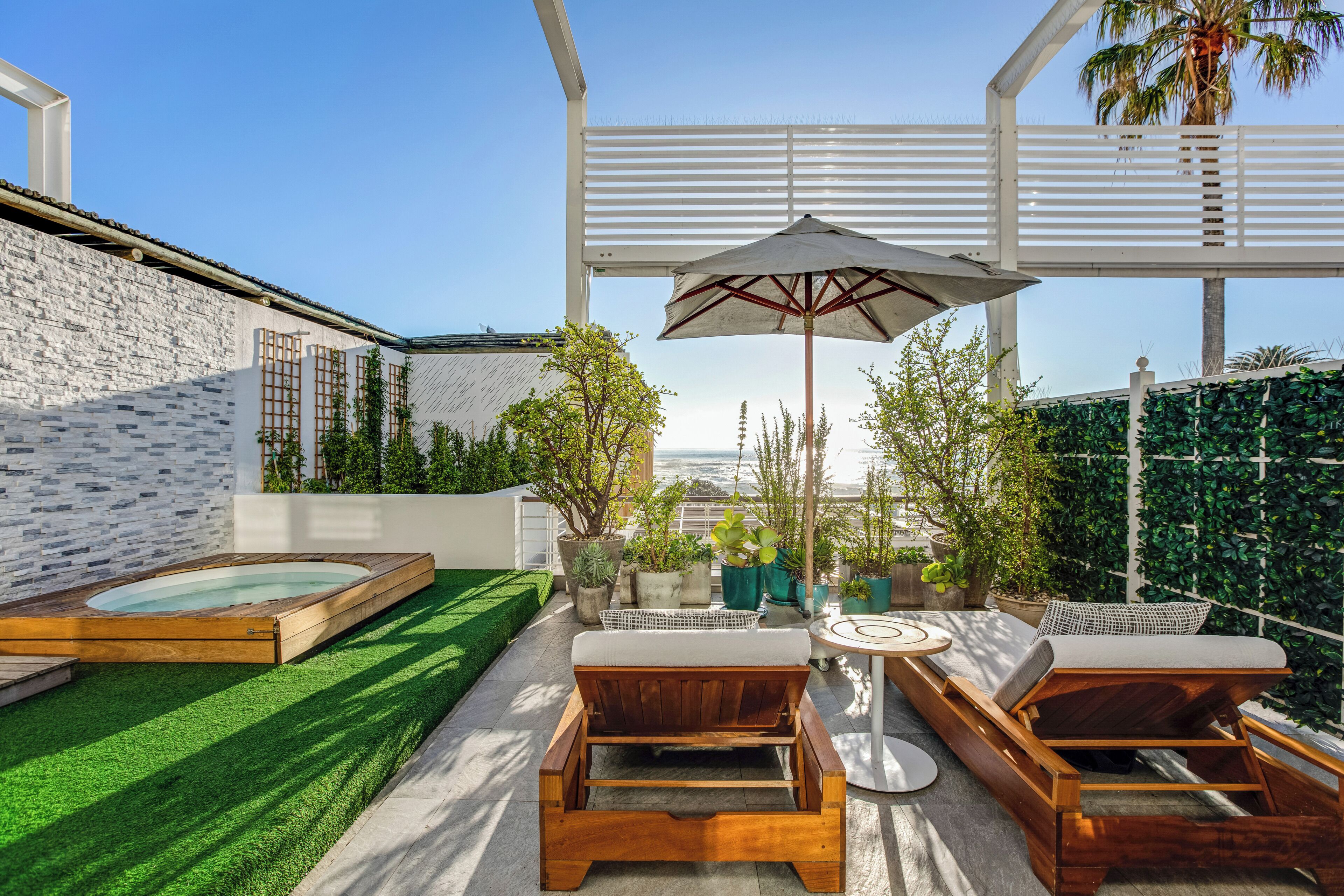 Une terrasse sur le toit équipée d’un jacuzzi, de chaises longues en bois et d’un grand parasol.